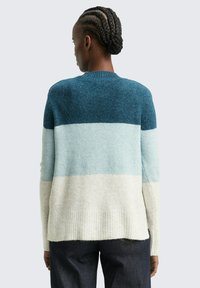 Pull en maille avec un col rond ; présente des rayures horizontales en bleu canard foncé, bleu clair et crème ; ourlet et poignets côtelés ; texture douce.
