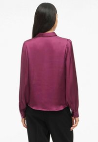Blusa de manga larga en satén morado intenso, con cuello y puños abotonados, con una textura lisa y brillante y un corte holgado.