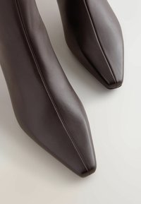 Bruine leren enkellaarsjes met een puntige neusdesign, een gladde textuur en nette naaddetails. Heeft een minimalistische esthetiek.