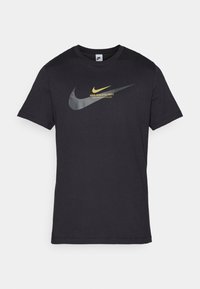 Černé tričko Nike, krátké rukávy, bavlněný materiál. Na přední straně se nachází velké šedé a zlaté logo swoosh s textem "NIKE ATHLETIC DEPT." nad ním.