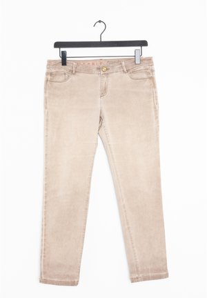 Beżowe jeansy slim-fit wiszące na czarnym wieszaku, z przednimi kieszeniami, szlufkami na pasek i zapięciem na guzik.