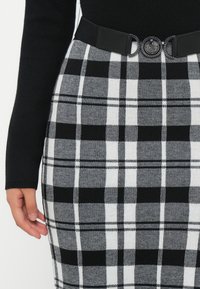Μαύρη και άσπρη καρό φούστα από υφασμάτινη ύφανση, με φαρδύ μαύρο ζωνάκι και κυκλική μεταλλική πόρπη.