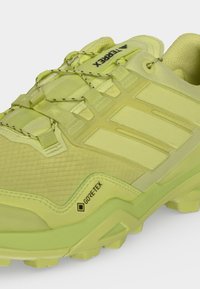 Κίτρινο ορειβατικό παπούτσι Adidas Terrex Gore-Tex με υφή στη σόλα, διχτάκια στο μπροστινό μέρος και λεπτομέρεια με το λογότυπο στη γλώσσα σε λευκό φόντο.