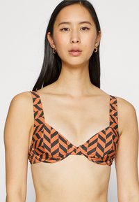 Sostenere con un motivo geometrico di zigzag arancioni e neri, con spalline larghe e chiusura sul retro, realizzato in tessuto morbido e elasticizzato.