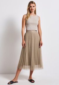 Vaalean beige pleatattu midi-hame, jossa on teksturoitu pinta ja leveä vyötärönauha. Yhdistetty kevyen, kiiltävän, ilman hihoja yläosan ja mustien liukusäätöjen kanssa.