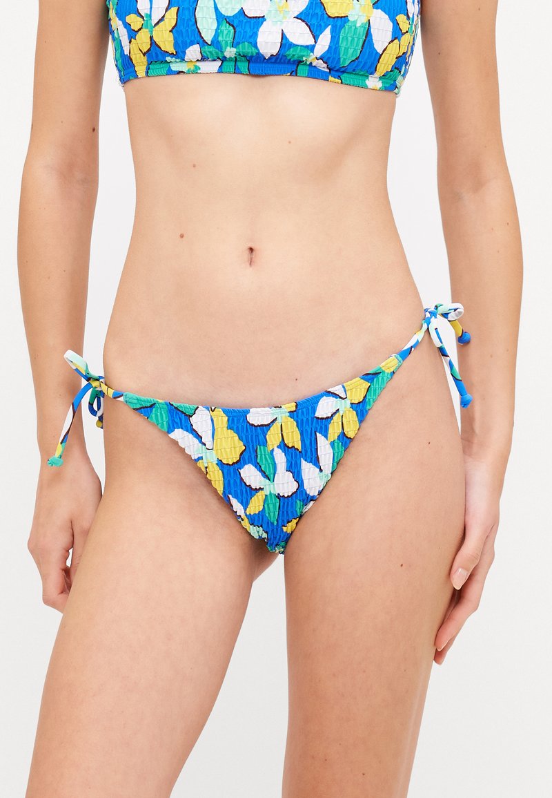 Virágmintás bikini alsó kék, sárga és fehér színben. Oldalt megkötőkkel rendelkezik és texturált mintázat jellemzi. Az anyag ráncolt kialakítású, amely szoros illeszkedést biztosít.
