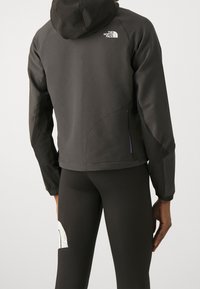 Bakvy av person som bär svart North Face-hoodie och svarta leggings med vitt mönster på vänster lår.