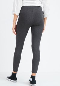 Grijze legging van een rekbare stof, met een slim fit en hoge tailleband. Draagt met zwarte hoge sneakers.