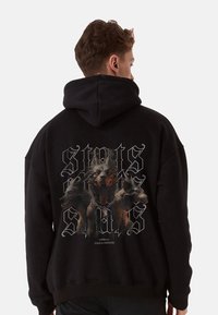 Black hoodie featuring a graphic of three dogs, one in front with a fierce expression. Includes stylized text and a chain design.