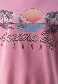 Pink t-shirt featuring a graphic design of palm trees, a sun setting over water, and the text "Panama Bay" in bold, black lettering.