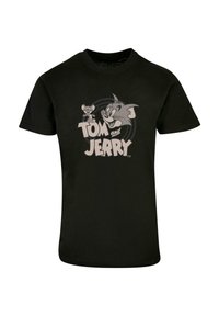 Must värvi puuvillane t-särk, millel on Tomi ja Jerry tegelased hallis trükis, allosas tekst "TOM ja JERRY", lihtsa tausta ees.