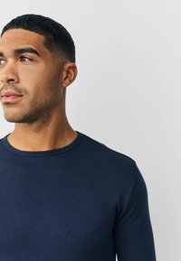 Marineblaue, gerippte Langarmshirt mit Rundhalsausschnitt, mit einer figurbetonten Passform und glatter Textur, getragen von einer Person, die leicht nach links blickt.