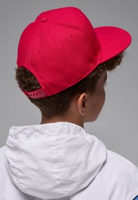 Red baseball cap with a flat brim and adjustable snapback, paired with a white hooded jacket featuring a textured fabric.