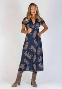 Maxiklänning i marinblått tyg med leopardmönster. V-ringning, korta ärmar, flödande form. Bärs med beiga mockahögklackade stövlar.