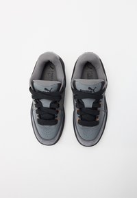 Un par de zapatillas Puma en gris y negro con cordones negros, ojales naranjas y un interior acolchado, vistas desde arriba sobre un fondo blanco.