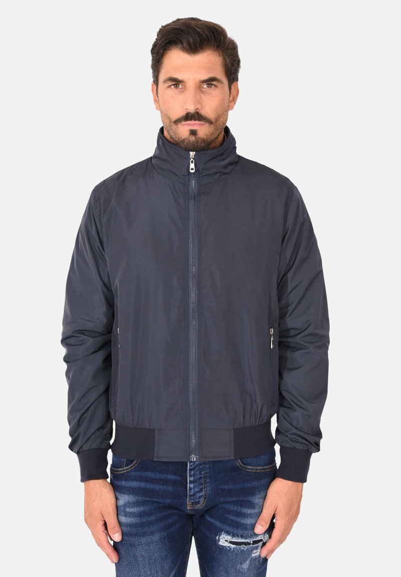 Giacca blu navy scura con colletto alto, zip frontale e polsini elasticizzati. Presenta una texture liscia e tasche laterali, progettata per un look aderente.