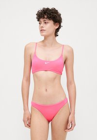Šviesiai rožinė bikini komplektas, pagamintas iš lygaus audinio. Viršus turi plonus dirželius ir mažą logotipą, o apačia pasižymi klasikiniu kirpimu.