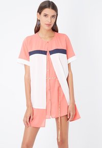 Vestido de botones en coral y blanco con mangas cortas, que presenta una franja horizontal azul marino, cintura ceñida con detalle de cadena y diseño en capas.