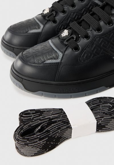 Black leather sneakers featuring a textured upper with geometric patterns and silver hardware. Includes braided black laces.