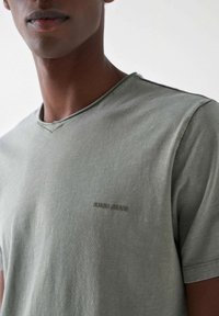 Světle zelené tričko s véčkovým výstřihem vyrobené z měkkého materiálu, které má jemnou texturovanou strukturu a malé reliéfní logo "Salsa Jeans" na hrudi.