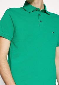 Polo vert en coton texturé avec un col, une patte de boutonnage à trois boutons et un petit logo sur la poitrine.