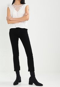 Biała bluzka z krótkim rękawem, zdobiona haftem kwiatowym i z przezroczystym dekoltem, w połączeniu z czarnymi obcisłymi dżinsami i botkami na kostkę z blokowym obcasem.