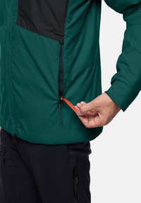 Leichte grüne Jacke mit schwarzen Akzenten, ausgestattet mit einer Reißverschlusstasche und einem orangefarbenen Ziehband. Glatte Textur und lässiges Design.