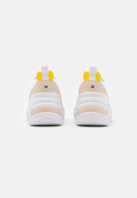 Weiße Sneaker mit einer strukturierten beige-gelben Akzentuierung an der Ferse. Verfügt über ein Logodetail auf der Rückseite und einen gepolsterten Kragen für zusätzlichen Komfort.