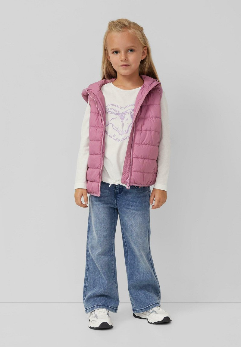 Pinker gepolsterter Weste mit Kapuze, über einem weißen Langarmshirt mit einem lila Pferdedruck getragen, kombiniert mit hellblauen weiten Jeans.