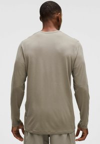 Hosszú ujjú ing világos bézs színű anyagból, egyszerű dizájnnal, kerek nyakkal, sima textúrával és oldalsó hasítékokkal az alján a szabad mozgás érdekében.