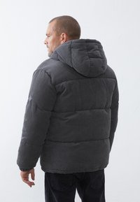 Graue Cordjacke mit Kapuze, ausgestattet mit einem gesteppten Design und gerippter Textur, von hinten betrachtet.