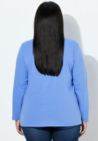 Blauw shirt met lange mouwen gemaakt van zachte stof, met een ontspannen pasvorm en een ronde hals, gecombineerd met een donkere spijkerbroek.