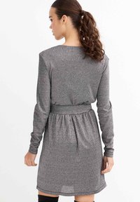 Vestido gris de manga larga con acabado texturizado, cintura con cinturón y falda acampanada. Presenta un escote redondo y mangas hasta la muñeca.