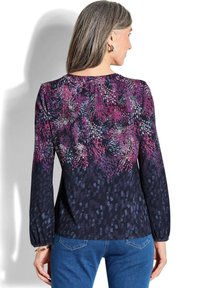 Langärmliges Oberteil mit dunklem Hintergrund und einem lebhaften Blumenmuster in lila, pink und blau. Hat einen runden Halsausschnitt und einen gerafften Detail.
