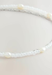 Õrn käevõru, millel on väikesed valged helmeste ja ebakorrapärase kujuga pärlitega hõbedast kett, hele tausta ees.