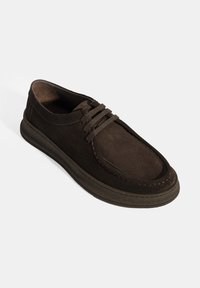 Chaussure en suede marron à lacets avec un bout arrondi, une tige texturée, une semelle rembourrée et un détail de surpiqûre contrastant le long des bords.