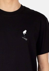 Zwarte katoenen t-shirt met een kleine witte grafiek van een hand en microfoon aan de linkerkant, met een standaard ronde hals.