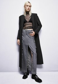 Cappotto lungo a righe nere sopra un top nero trasparente, abbinato a una gonna di denim grigia con tasche cargo e un'alta spaccatura. Scarpe platform nere.