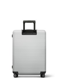 Valise rigide argentée avec des rainures horizontales, roues noires et une poignée rétractable, affichant un design rectangulaire élégant.