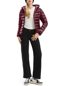 Burgundrote gepolsterte Jacke mit Kapuze, Reißverschluss und elastischen Bündchen, kombiniert mit einem weißen Langarmoberteil und schwarzen weit geschnittenen Jeans.