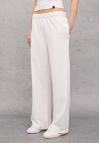 Witte zwemshorts gemaakt van zacht materiaal met een elastische tailleband, zijzakken en een ontspannen, wijde pasvorm. Gestreepte accenten aan de zoom.