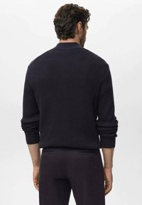 Navy geribbelde gebreide trui met een ronde hals, voorzien van lange mouwen en opgerolde manchetten. Eenvoudig ontwerp aan de achterkant; combineert comfort en textuur.