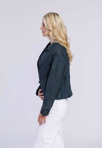 Donkerblauwe leren jas met een kraag, sluiting met knopen aan de voorkant en twee borstzakken, gecombineerd met witte broek. Casual pasvorm met een gladde textuur.