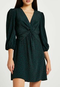 Vestido de manga corta en verde oscuro con estampado de leopardo negro, con un escote en V profundo y un detalle de recogido en la cintura. Tejido suave.
