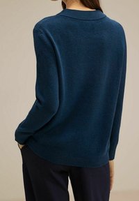 Mörkblå stickad tröja med rund krage, långa ärmar och avslappnad passform. Mjuk textur med ribbade muddar och nederkant. Bakvy visas.