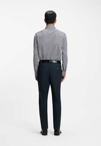 Gestreept overhemd met knopen en lange mouwen; donkere broek; zwarte riem; stijlvolle schoenen. Het overhemd heeft dunne marineblauwe en witte strepen.