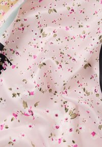 Ροζ μεταξένιο ύφασμα με μικρά λευκά και φωτεινά ροζ λουλούδια και πράσινα φύλλα, απαλά τσαλακωμένο.