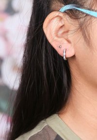 Zilveren ring oorbel met een gestructureerde afwerking en een kleine studs in het oorlellen. Haar dat gedeeltelijk het oor bedekt, met een zachte huidtextuur.