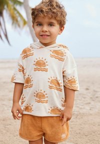Kortærmet, cremefarvet hoodie med sol- og bølgedesign i orange, parret med matchende bløde frottéshorts. Teksturert, afslappet look.