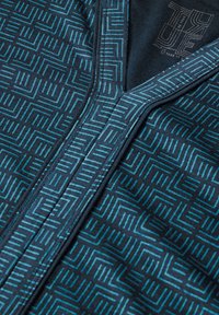 Navyfarbener Stoff-Reißverschluss-Pullover mit einem geometrischen türkisfarbenen Muster. Glatte Textur mit einem strukturierten Kragen und sichtbaren Stecknähten.